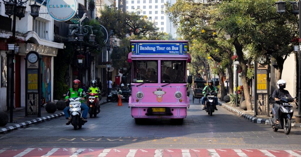 Vibrant pink tour bus and motorcyclists on a busy street in Bandung, Indonesia.